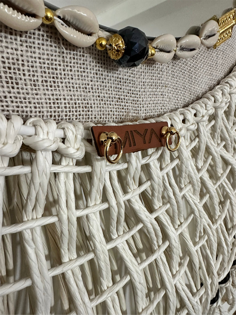 Détail d’un miroir MIYA en fibres naturelles et macramé avec cauris, perles et plaque en cuir.